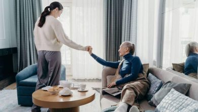 Younger woman holding hands with an older woman sitting on a sofa at home