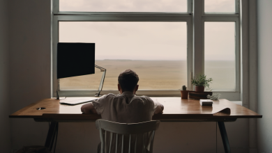 AI-generated image: A man is seated at a wooden desk in a room with a large window.