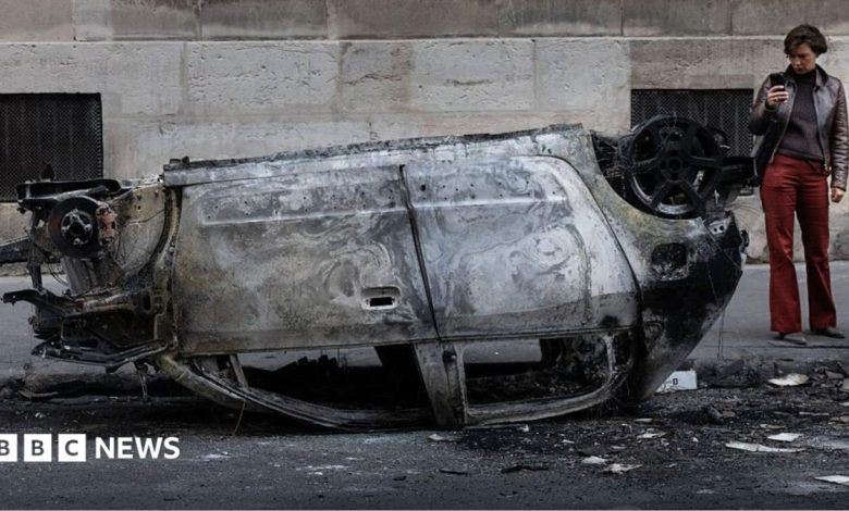 A woman takes a photo of the wreckage of a burnt-out car in central Paris