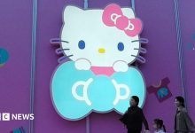 Three women walk past a big glowing Hello Kitty signage on a purple store wall in Shanghai, China