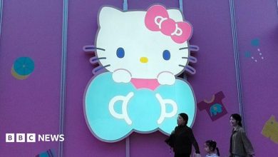Three women walk past a big glowing Hello Kitty signage on a purple store wall in Shanghai, China