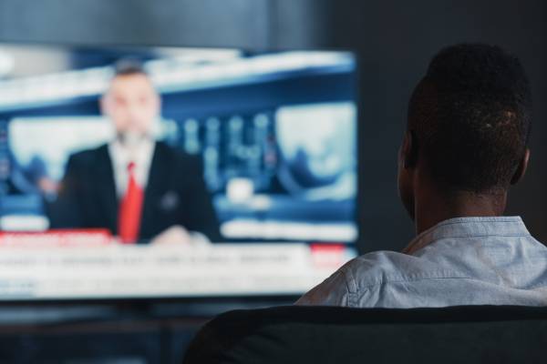 Back of man's head watching newscaster on TV