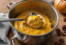 AI-generated image: A stainless steel pot filled with orange-colored mashed pumpkin is the main subject.