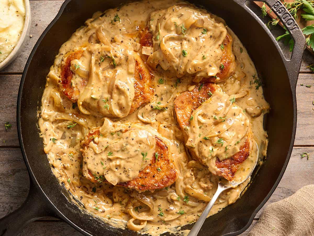 Overhead view of smothered pork chops in a skillet.
