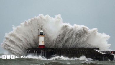 A wave crashes dramatically over a lighthouse
