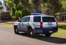AI-generated image: A white police vehicle, with blue lights on the roof and a ‘POLICE’ sign on the side, is parked on an asphalt road.